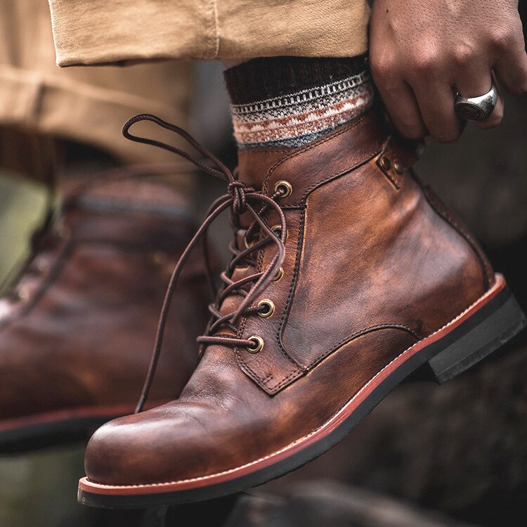 Brown leather lace-up boots with rugged design, worn with patterned socks and beige pants. Perfect for outdoor adventures and casual fashion.