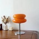 Orange modern table lamp with glossy finish on a wooden surface, next to decorative vases. Contemporary home decor lighting, minimalist design.