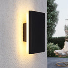 Modern black outdoor wall light fixture with warm LED glow, mounted on textured concrete wall, ideal for garden or patio lighting.