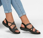 Women's black strappy sandals with cushioned soles, worn with light blue skinny jeans. Comfortable summer footwear, casual style.