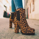 Leopard print high heel ankle boots with chunky platform sole, worn with blue jeans on an urban street. Fashion footwear, trendy style.