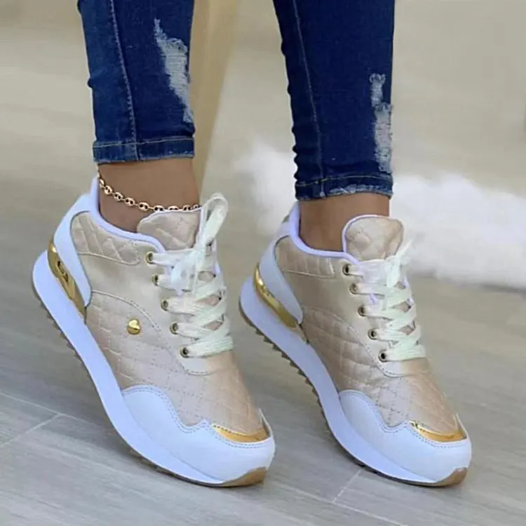 Stylish gold and white women's sneakers with quilted design, lace-up closure, and metallic accents, paired with ripped jeans on wooden floor.