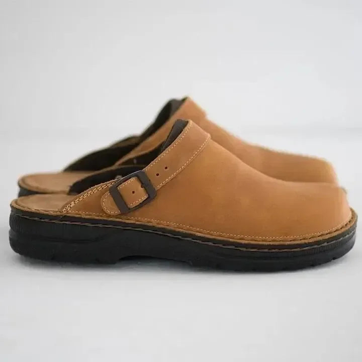 Brown leather clogs with adjustable strap and black sole, side view. Comfortable slip-on footwear for casual wear. Durable and stylish design.