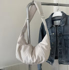 White hobo bag hanging on a metal rack beside a denim jacket. Stylish, minimalist fashion accessory, perfect for casual and chic outfits.