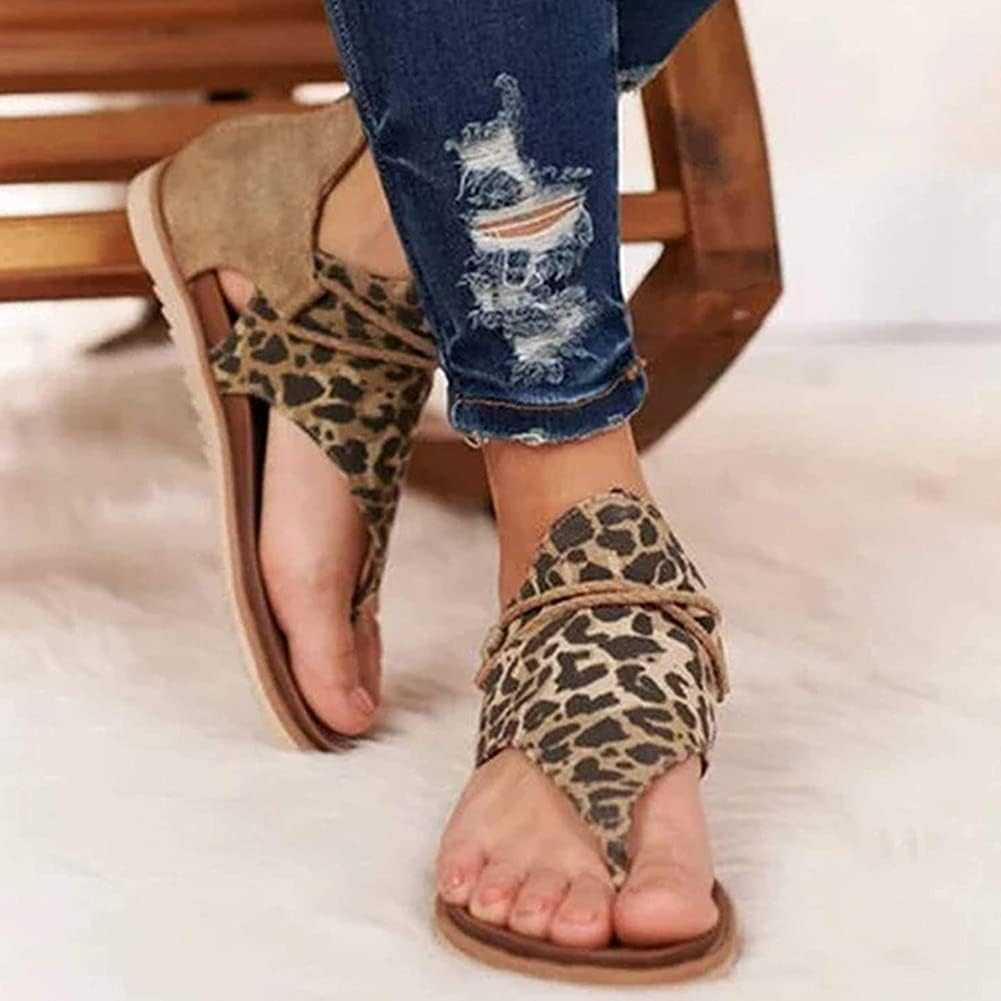 Leopard print women's sandals with open toe design, paired with distressed denim jeans, on a white fluffy rug. Fashionable summer footwear.