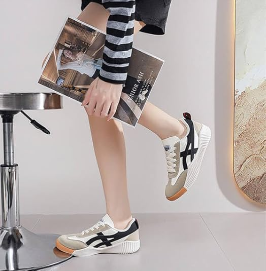 Casual sneakers with black stripes and beige accents, worn by a person in a striped outfit, holding a magazine. Stylish footwear, modern fashion.