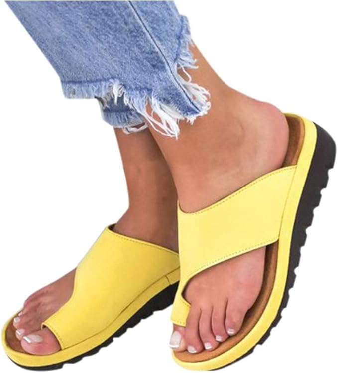 Yellow slip-on sandals with black soles, worn by a person in frayed blue jeans. Comfortable summer footwear, casual style, open-toe design.