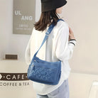 Woman wearing a stylish blue crossbody bag with woven design, paired with a white blouse and black hat, standing in a modern cafe setting.