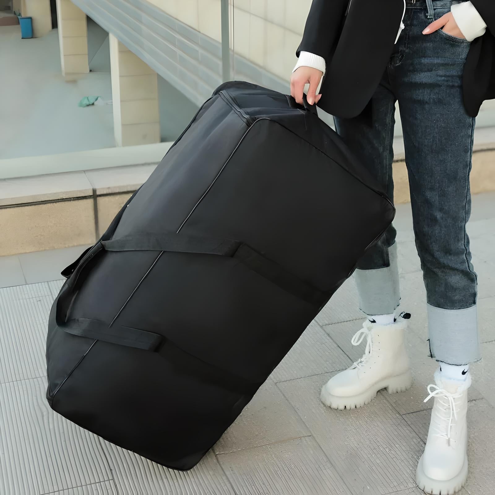 Person holding large black travel duffel bag with handles, wearing casual jeans and white boots. Ideal for luggage, travel, and storage needs.