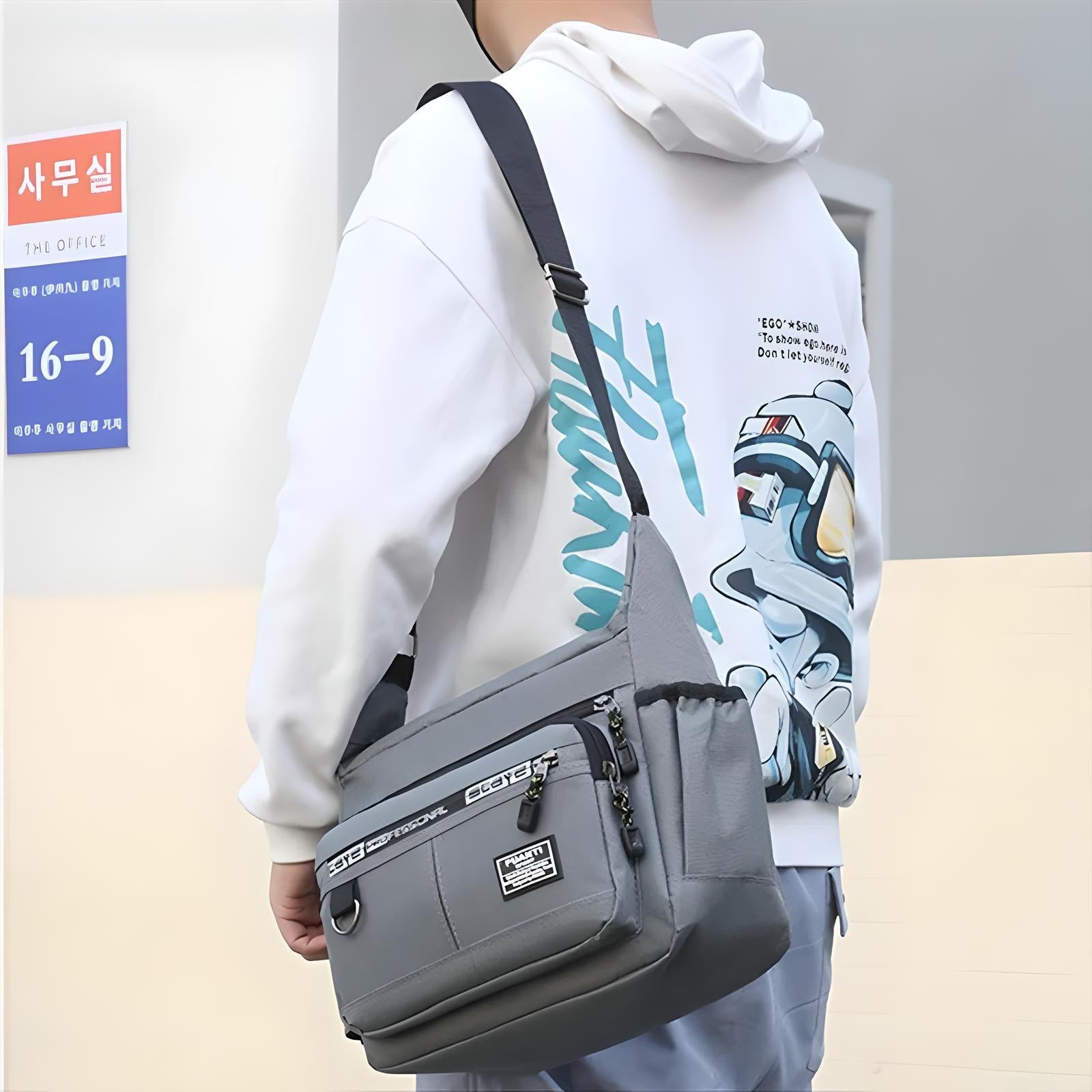 Man wearing a white graphic hoodie and carrying a stylish gray crossbody messenger bag with multiple pockets, standing near an office sign.