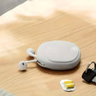 White wireless earbuds in a sleek charging case on a wooden table, accompanied by a key and yellow earplugs. Modern tech accessories.