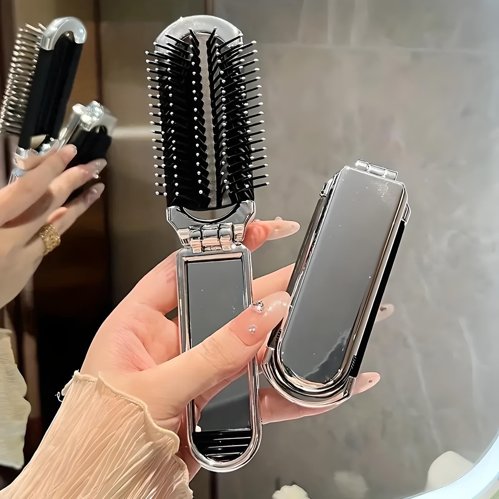 Dual-sided hairbrush and mirror set with sleek black and silver design, held by a hand with manicured nails, ideal for travel and styling.