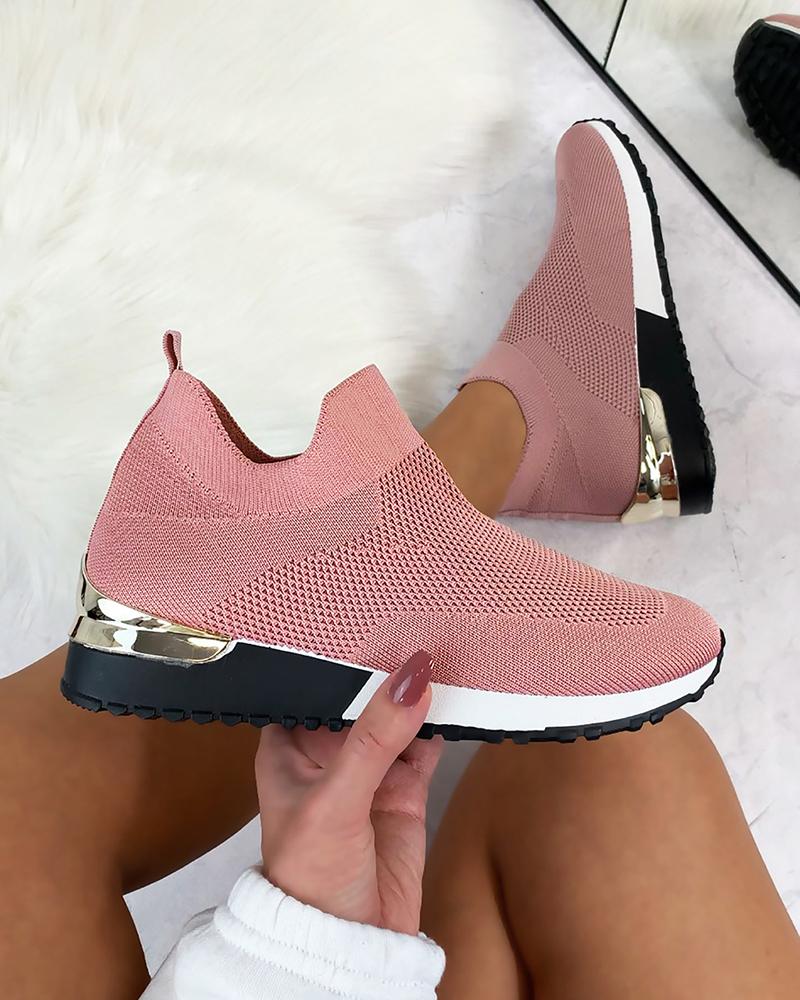 Pink slip-on sneakers with knit upper, white sole, and metallic heel detail, held by a person with manicured nails. Fashionable women's footwear.