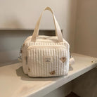 Quilted white diaper bag with hedgehog print, dual handles, and adjustable strap on a shelf. Ideal for baby essentials. Stylish and functional design.