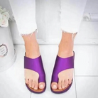 Purple open-toe sandals on feet, paired with white frayed jeans, on a white tiled floor. Fashionable summer footwear, casual style.