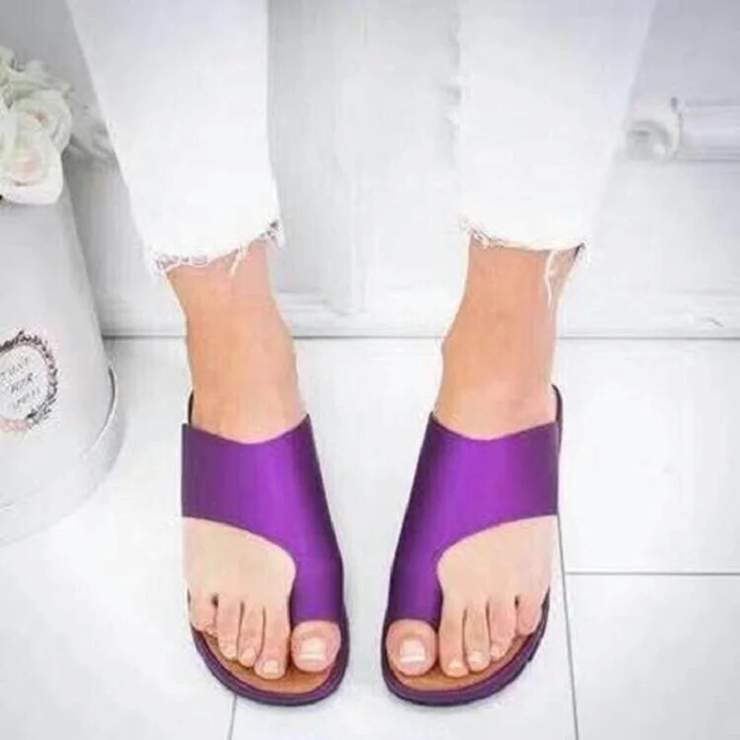 Purple open-toe sandals on feet, paired with white frayed jeans, on a white tiled floor. Fashionable summer footwear, casual style.