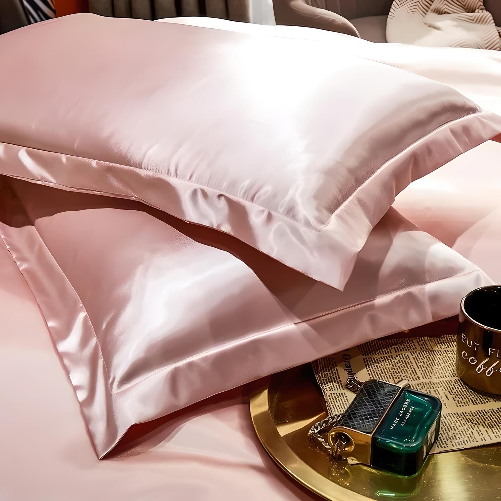 Luxurious pink silk pillowcases on a bed, reflecting light, with a gold tray holding a perfume bottle and coffee mug nearby. Perfect for elegant bedroom decor.