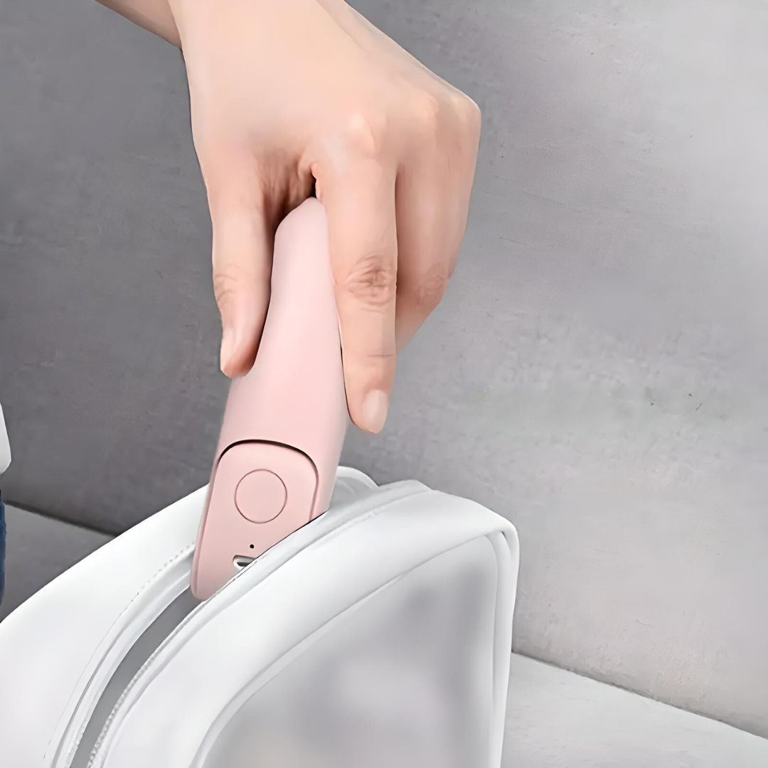 Hand placing a pink portable lint remover into a white travel bag. Compact fabric shaver for clothes, ideal for travel and home use.