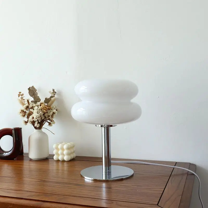 Modern white glass table lamp with chrome base on wooden desk, accompanied by decorative vases and dried flowers, minimalist home decor.