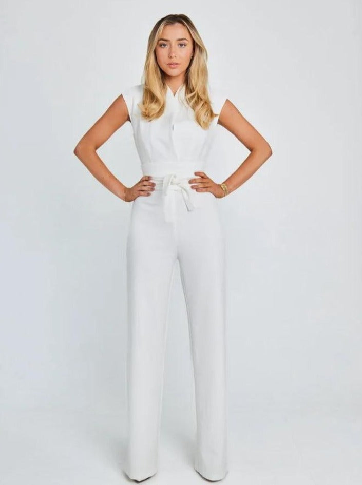 Woman in elegant white jumpsuit with cap sleeves and belted waist, standing confidently against a plain background. Fashion, style, women's clothing.