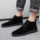 Black suede men's ankle boots with laces, worn with rolled-up jeans, on a gray carpet. Stylish casual footwear for men, perfect for fall fashion.