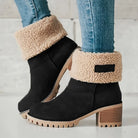 Black suede ankle boots with faux fur lining, chunky wooden heel, and lug sole, paired with blue jeans. Stylish winter footwear for women.