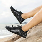 Black minimalist barefoot running shoes on rocky beach, showcasing lightweight design and flexible sole. Perfect for outdoor fitness and trail running.