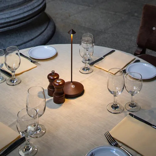 Elegant dining table setup with modern table lamp, wine glasses, and pepper mills on a round table, perfect for upscale restaurant ambiance.