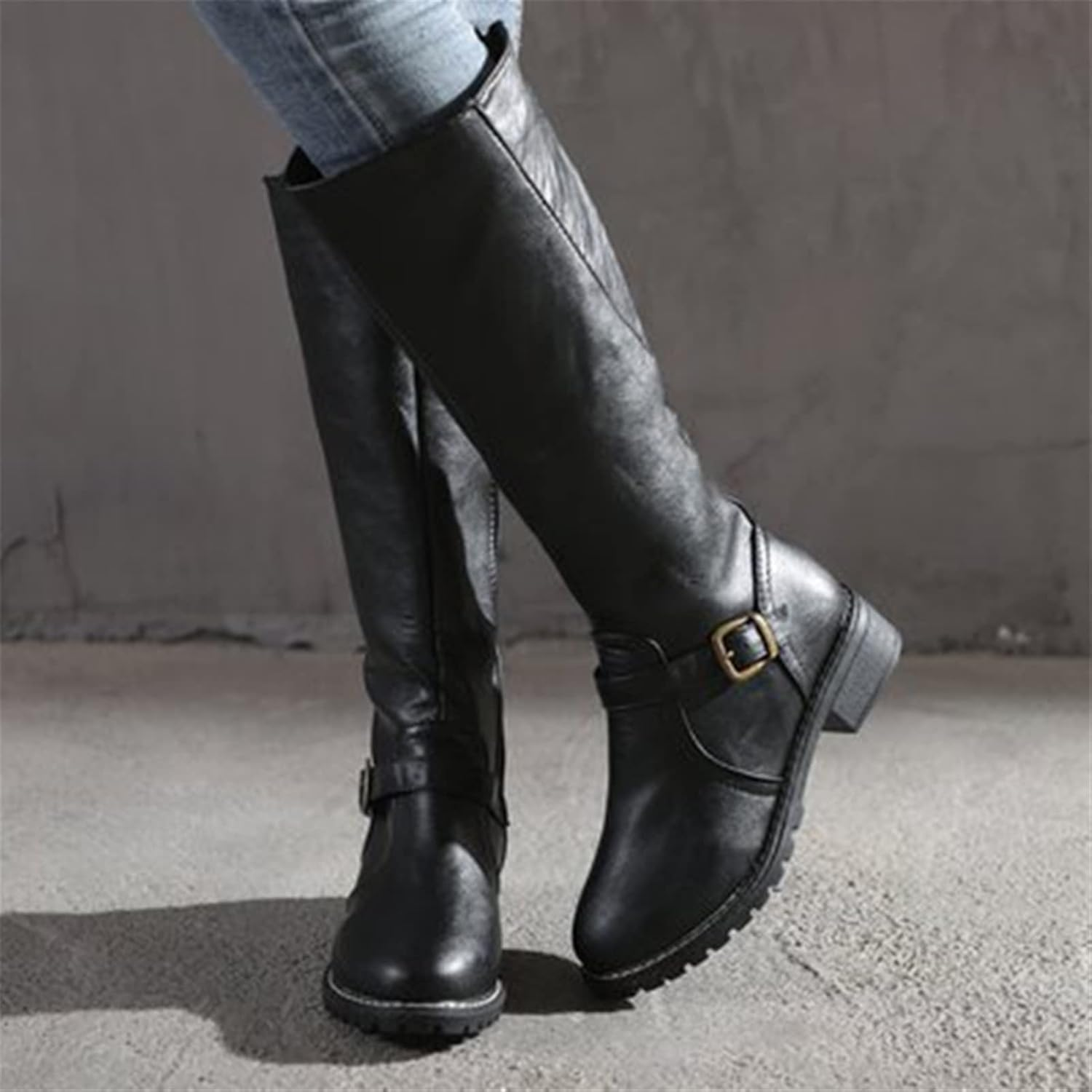 Black knee-high leather boots with buckle detail, worn with jeans. Stylish women's footwear, perfect for fall fashion and casual outfits.