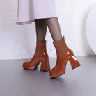 Brown patent leather platform ankle boots with chunky heels and ribbed knit sock detail, worn with a light pink skirt. Fashionable women's footwear.