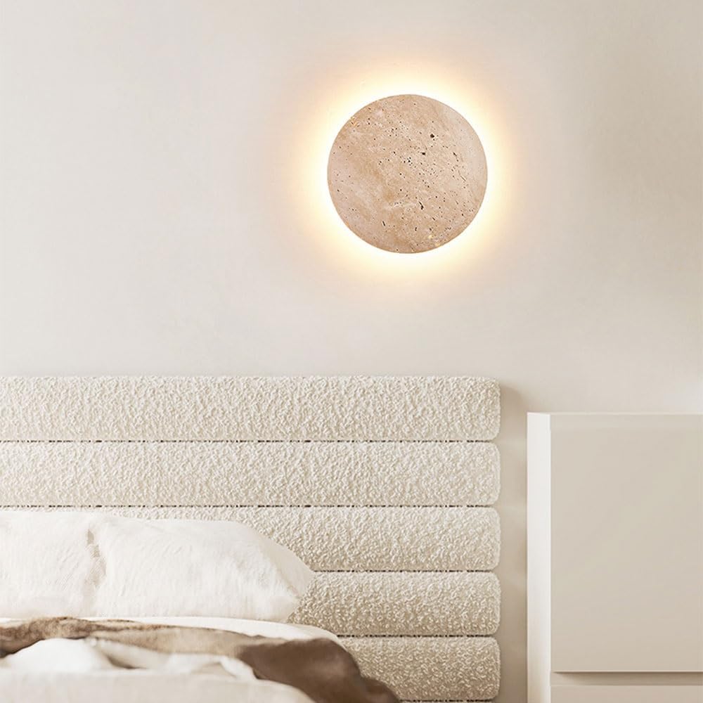 Modern round wall sconce with warm LED lighting, mounted on a textured beige wall above a minimalist bed. Ideal for contemporary bedroom decor.