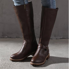 Brown leather knee-high boots with side zipper and buckle detail, worn with jeans. Stylish women's footwear, perfect for fall fashion and outdoor wear.