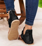 Black open-toe sandals with back zipper, worn with blue jeans, on a soft white rug. Fashionable women's footwear, casual style, comfortable design.