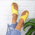 Yellow open-toe sandals on feet, paired with ripped blue jeans, against a white brick background. Stylish summer footwear, casual fashion.