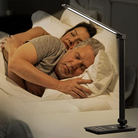 Couple sleeping under LED desk lamp with adjustable arm, touch control, and USB charging port. Modern bedside lighting, energy-efficient lamp.