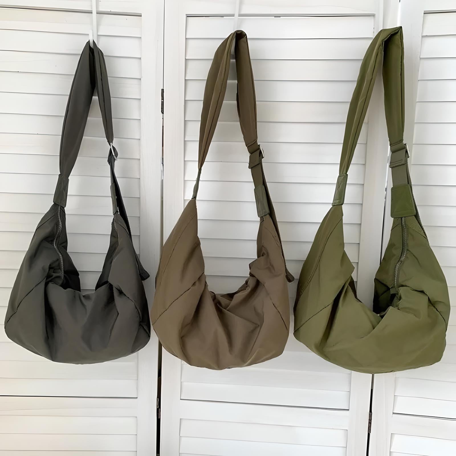 Three stylish, slouchy hobo bags in dark green, taupe, and olive hang against a white shutter backdrop. Perfect for casual fashion and versatile use.