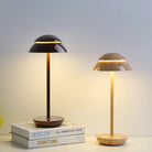 Modern wooden table lamps with dome-shaped shades on a stack of decor and furniture books, illuminating a minimalist interior setting.