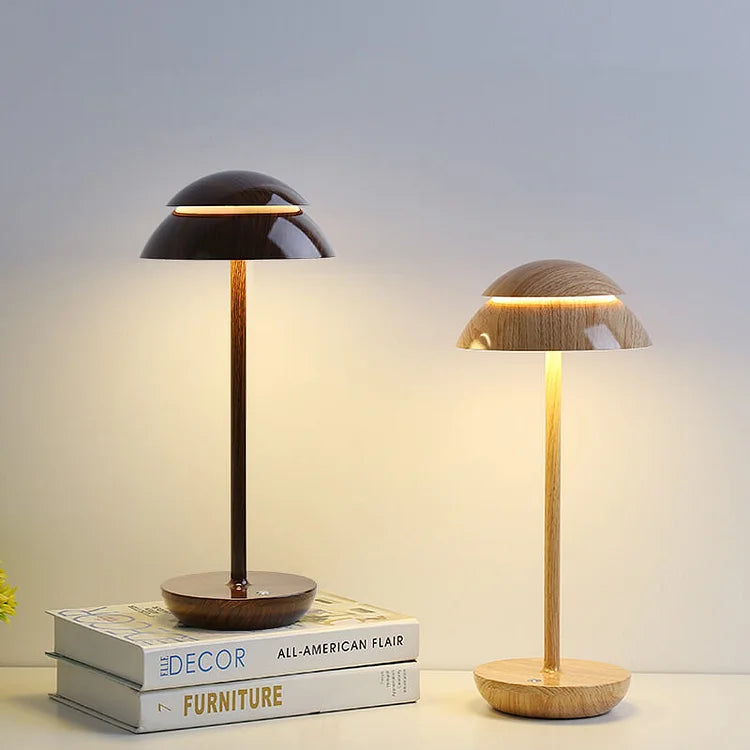 Modern wooden table lamps with dome-shaped shades on a stack of decor and furniture books, illuminating a minimalist interior setting.