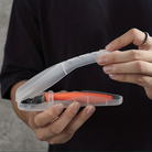 Person holding a transparent plastic case with an orange-handled razor inside, showcasing portable grooming tools, travel-friendly shaving kit.