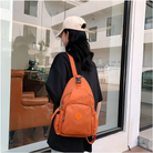 Woman wearing a black t-shirt and beige cap with an orange backpack standing outside a modern cafe. Fashionable casual outfit, urban style.