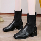 Black leather ankle boots with ribbed knit upper, block heels, and square toe design on wooden floor. Fashionable women's footwear.