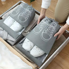 Person packing white sneakers in gray shoe bags into a suitcase; travel organization, efficient packing, shoe storage, travel essentials.