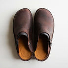 Brown leather slip-on clogs with buckle detail on white background, showcasing rustic footwear design, comfortable casual shoes for men and women.