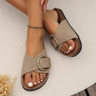 Woman's feet wearing stylish beige sandals with large buckle on a textured rug, showcasing trendy summer footwear and pedicure fashion.