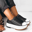 Black and white platform sneakers with chunky soles, worn with rolled-up black pants. Trendy footwear for casual fashion and street style.