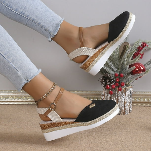 Women's black espadrille wedge sandals with ankle strap, paired with light blue jeans. Fashionable summer footwear, casual chic style.