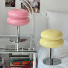 Modern pink and yellow macaron-shaped table lamps on a glass bedside table, featuring sleek chrome bases, ideal for contemporary home decor.