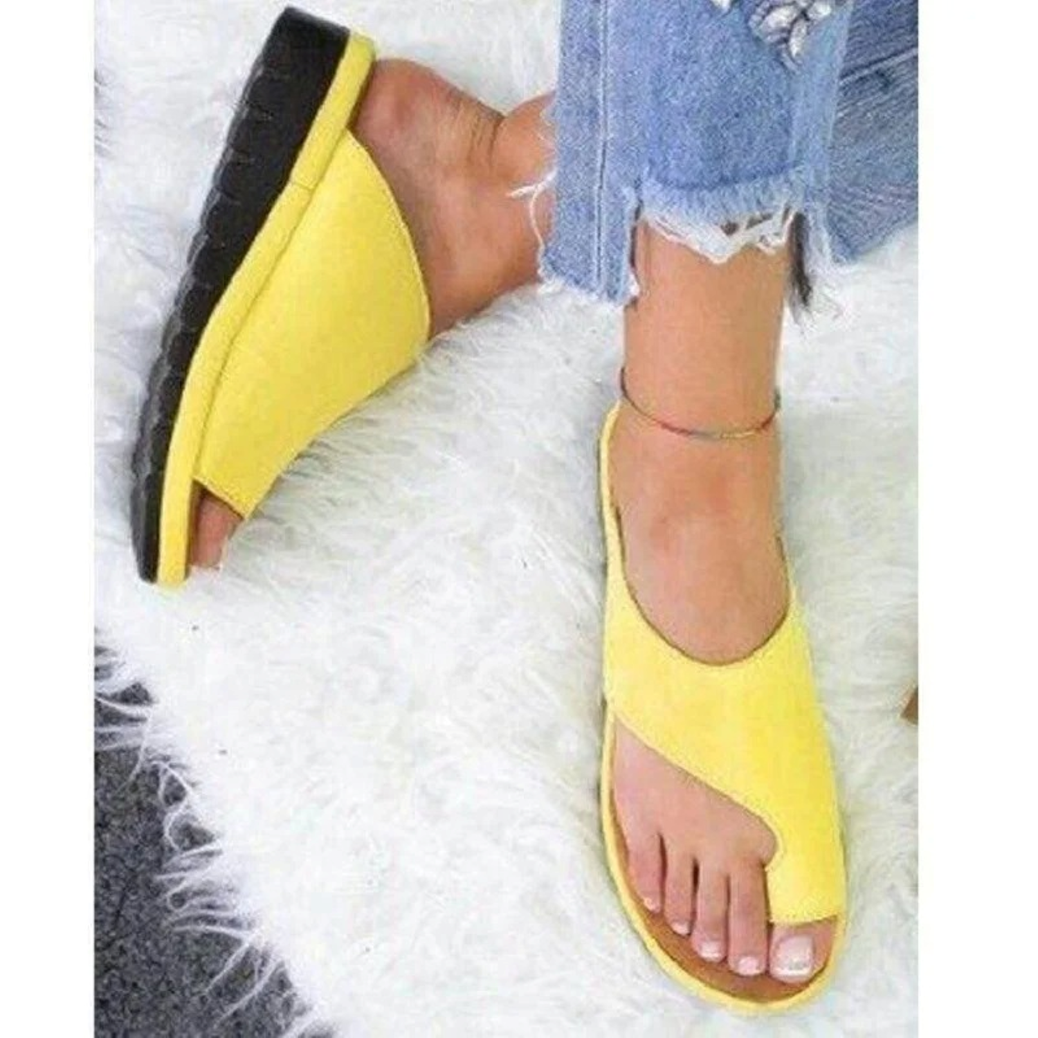 Yellow open-toe wedge sandals on a woman's feet, paired with frayed hem jeans, resting on a white fluffy rug. Fashionable summer footwear.