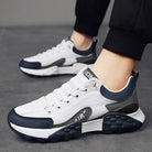 White and navy blue athletic sneakers with cushioned soles, worn by a person in black pants, ideal for running and casual wear.