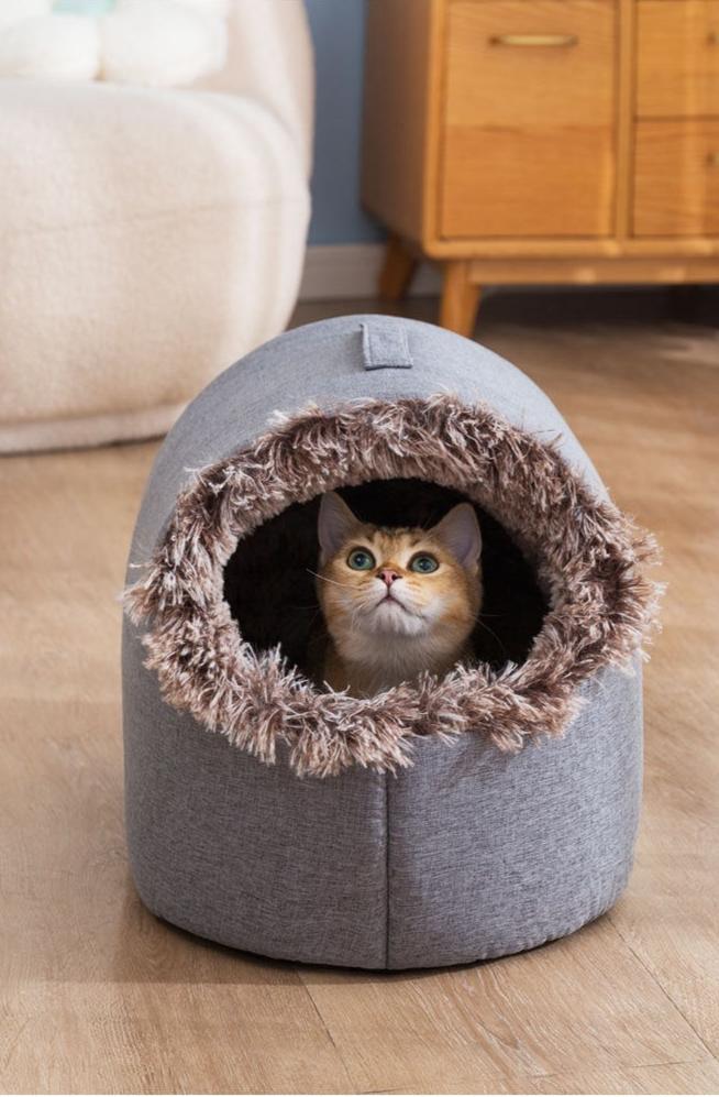 Cute cat peeking from cozy gray pet bed with faux fur trim, wooden furniture background. Perfect for pet lovers, home decor, cat accessories.